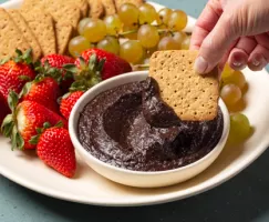 Bol de houmous au chocolat sur un plateau avec des biscuits Graham, des figues, des fraises et des raisins
