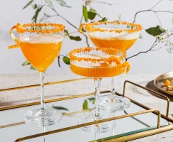 Trois verres de cocktail pétillant au gingembre et au curcuma garnis d'écorces d'orange et bordés de sucre