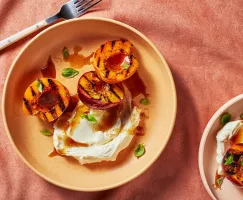 Deux bols remplis de moitiés de pêches grillées avec une garniture de mascarpone et de basilic, et un filet de glaçure à la cass