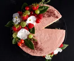 Gâteau avec meringue suisse crème au beurre rose, disposé sur une assiette à gâteau et décoré de fleurs, de verdure et de petits