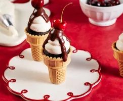 Cupcakes au chocolat dans des cornets à glace classiques, décorés de glaçage, de ganache au chocolat et garnis d'une cerise, ser