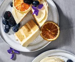 Un mini-gâteau au citron et à la camomille sur une assiette avec une tranche coupée, servi avec des baies et garni de baies