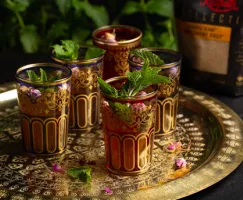 Cinq verres colorés remplis de thé marocain à la menthe, décorés de feuilles de menthe et disposés sur un plateau doré