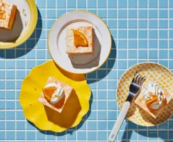 Quatre morceaux de gâteau glacé à la vanille et à l'orange dans des assiettes sur un comptoir carrelé bleu.