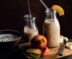 Deux bouteilles d’une portion de smoothie banane, pêche et Earl Grey avec pailles en verre, une planche à découper et des fruits