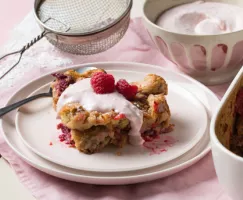 Une assiette présentant une portion de pouding au pain avec de la crème et des framboises