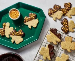 Des biscuits à la menthe en forme de trèfle trempés dans le chocolat et parés de paillettes dorées, disposés sur un plateau vert