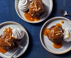 Vue de haut en bas de trois sticky toffee puddings sur des assiettes, chacun avec une cuillerée de crème fouettée et de sauce