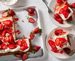 Un gâteau en plaque fraise-yuzu sur un plateau blanc servi avec des fraises avec deux tranches sur des assiettes.