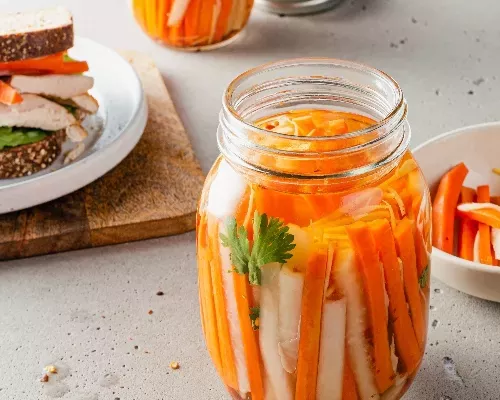 Un bocal de carottes et de radis daikon marinés avec un sandwich en arrière-plan
