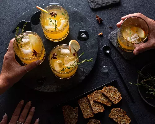 Mains approchant des verres de cocktail à la pomme et aux épices pour tarte à la citrouille servies avec des craquelins