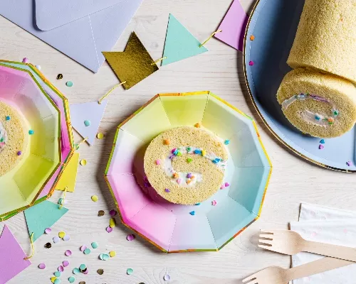 Roulé de gâteau blanc sur une assiette, trois tranches coupées sur des assiettes ombré arc-en-ciel avec des fourchettes en bois